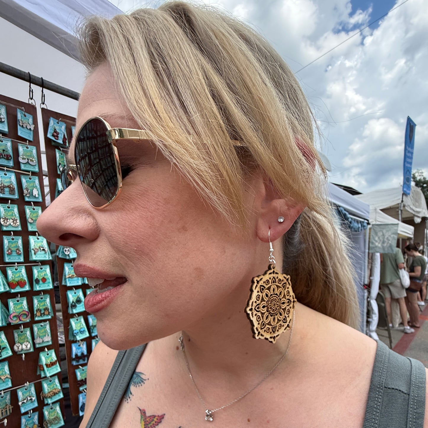 Customer wearing handcrafted wooden mandala dangle earrings at an outdoor art festival. This lifestyle photo showcases the size, movement, and elegant detail of these lightweight geometric earrings with hypoallergenic .925 sterling silver hooks. A beautiful accessory for bohemian style, everyday wear, festivals, and nature-inspired wardrobes.