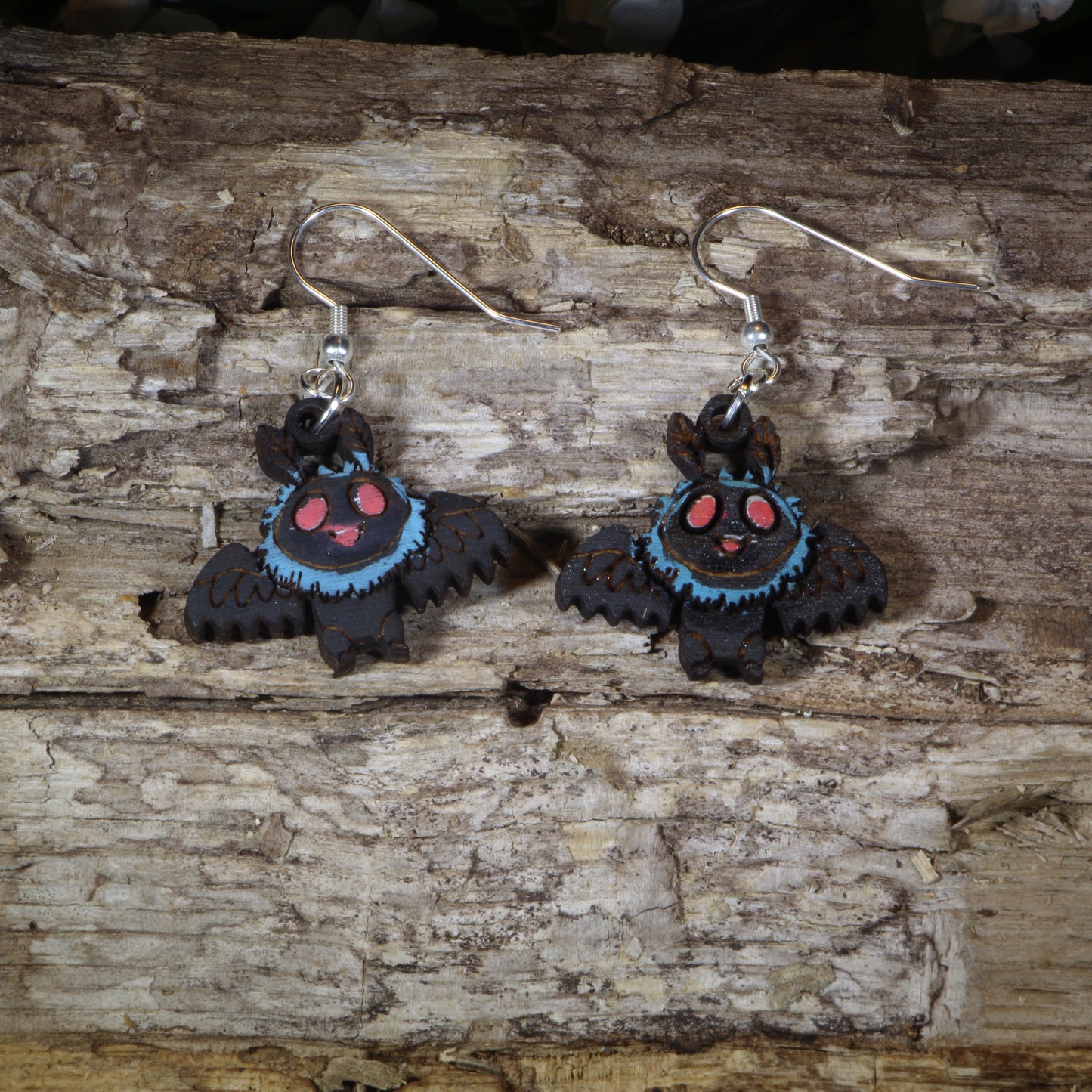 Hand-painted wooden cute Mothman dangle earrings featuring an adorable winged cryptid with glowing red eyes, hypoallergenic sterling silver hooks, and lightweight cryptid mythology jewelry for folklore fans and paranormal enthusiasts by Cate's Concepts.