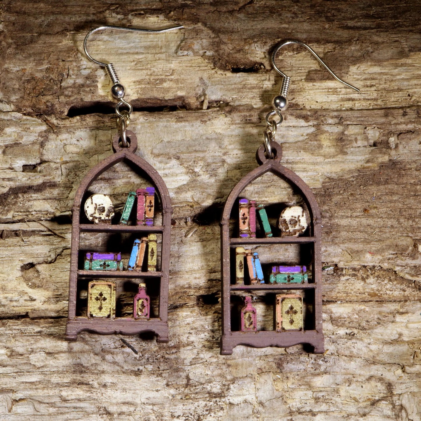 Handcrafted Oddities Bookshelf wooden dangle earrings featuring a detailed bookshelf filled with skulls, potion bottles, vintage books, mushrooms, curiosities, and mystical treasures. Lightweight laser-cut wooden earrings with hypoallergenic .925 sterling silver hooks, perfect for gothic jewelry lovers, dark academia enthusiasts, librarians, bookworms, Halloween fans, and collectors of oddities.