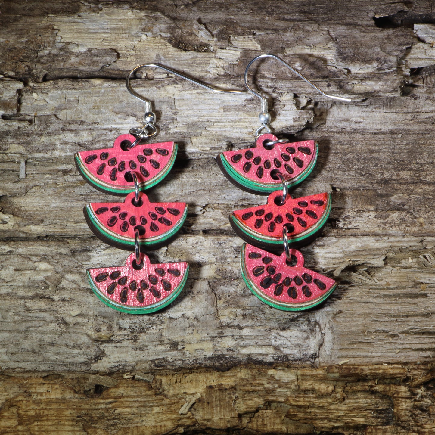 Hand-painted wooden watermelon slice cascade dangle earrings featuring layered juicy watermelon wedges with vibrant red, green, and black seed details. Crafted from lightweight wood with hypoallergenic .925 sterling silver hooks, these eye-catching earrings are perfect for summer fashion, fruit lovers, beach vacations, farmers markets, picnics, and anyone who enjoys bold food-inspired statement jewelry.