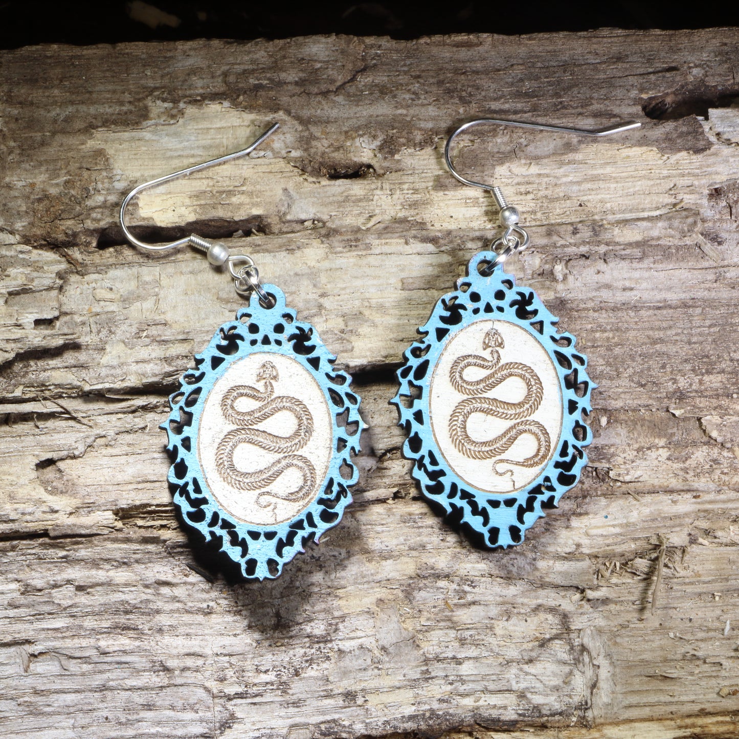 Handcrafted Light blue framed snake wooden dangle earrings featuring a detailed serpent coiled within an ornate gothic-inspired frame. Lightweight laser-cut wooden earrings with hypoallergenic .925 sterling silver hooks, perfect for snake lovers, gothic fashion, reptile enthusiasts, witchy style, dark academia, and nature-inspired handmade jewelry.