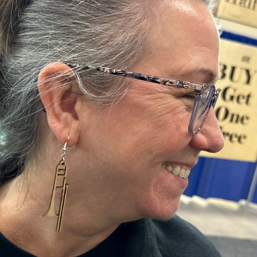 Close-up of a person wearing glasses with a trombone-wooden-dangle-earring.