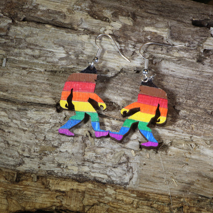 Hand-painted wooden rainbow pride Bigfoot dangle earrings featuring a colorful Sasquatch silhouette with rainbow stripes, hypoallergenic sterling silver hooks, and lightweight LGBTQ+ cryptid jewelry for pride celebrations and Bigfoot fans by Cate's Concepts