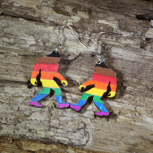 Hand-painted wooden rainbow pride Bigfoot dangle earrings featuring a colorful Sasquatch silhouette with rainbow stripes, hypoallergenic sterling silver hooks, and lightweight LGBTQ+ cryptid jewelry for pride celebrations and Bigfoot fans by Cate's Concepts