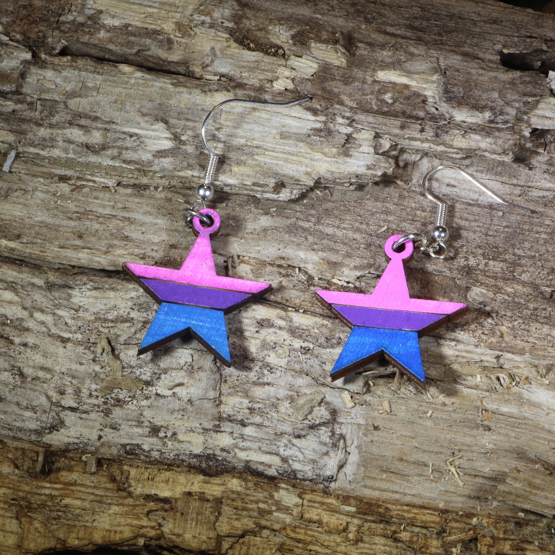 Hand-painted wooden bisexual pride star dangle earrings featuring pink, purple, and blue bisexual flag stripes, hypoallergenic sterling silver hooks, and lightweight LGBTQ+ pride jewelry for bisexual pride celebrations and queer accessory lovers by Cate's Concepts.
