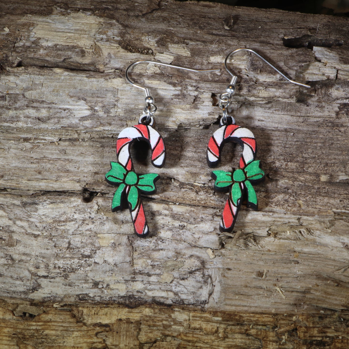 Hand-painted wooden candy cane with bow dangle earrings featuring festive red and white candy canes accented with a holiday bow, hypoallergenic sterling silver hooks, and lightweight Christmas jewelry for holiday celebrations by Cate's Concepts.