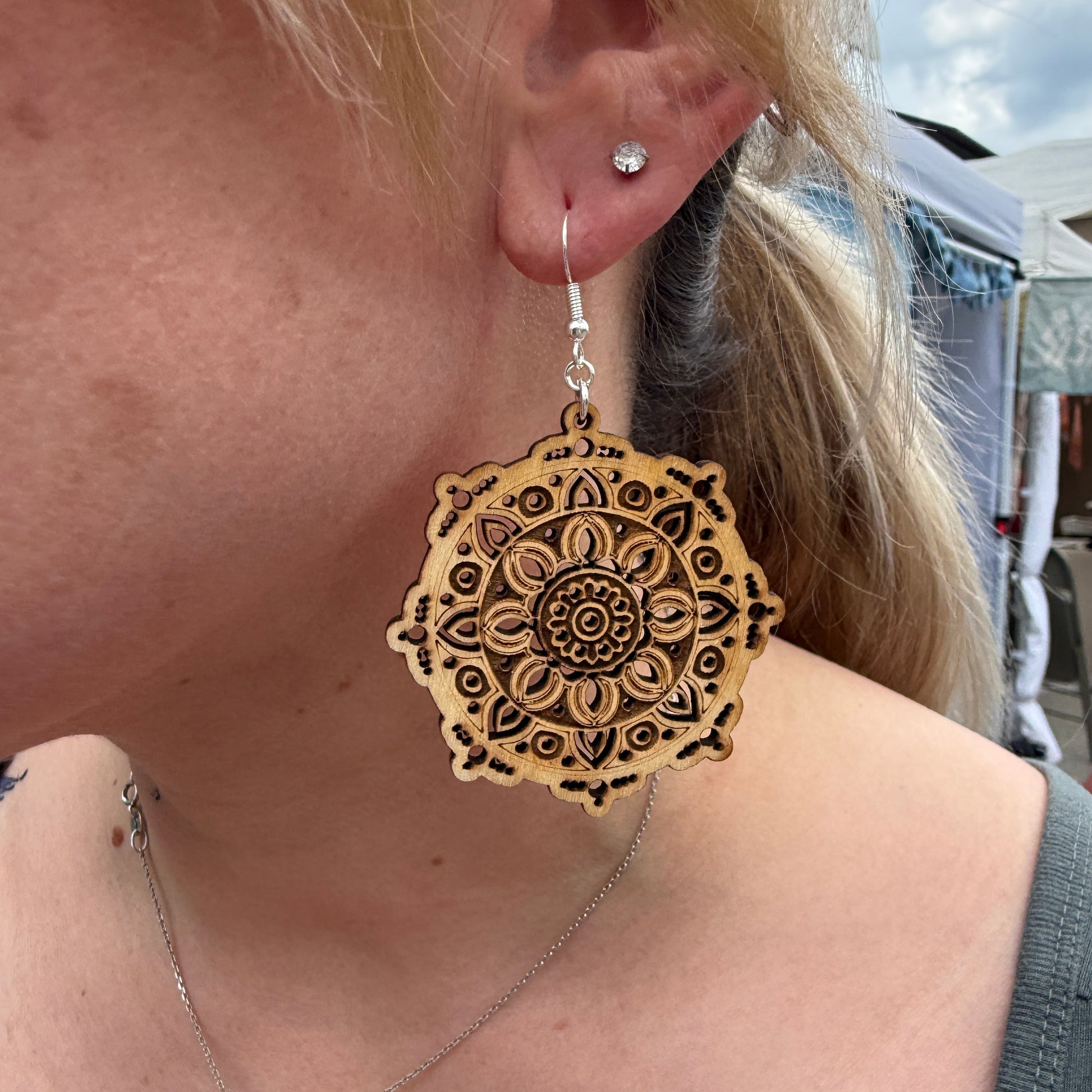 Close-up of a customer wearing intricate laser-cut wooden mandala dangle earrings. This lifestyle photo highlights the detailed geometric design, natural wood finish, lightweight construction, and hypoallergenic .925 sterling silver hooks. Perfect for boho fashion lovers, yoga enthusiasts, meditation practitioners, and anyone who appreciates artisan-inspired jewelry.