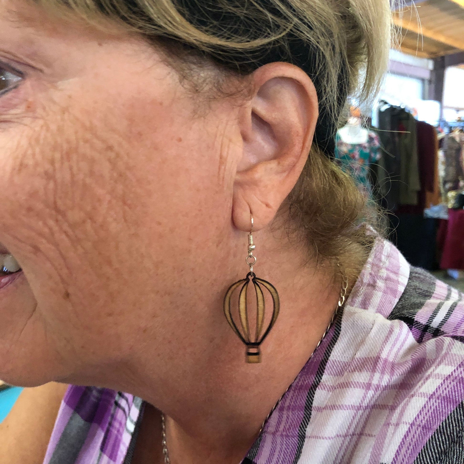 Close-up of handmade wooden hot air balloon dangle earrings worn on hypoallergenic .925 sterling silver hooks. Lightweight travel-inspired earrings featuring an open-cut balloon design, shown worn for size and scale, perfect for adventure lovers and hot air balloon enthusiasts.