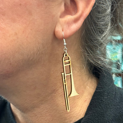 Close-up of handmade wooden trombone dangle earring worn on hypoallergenic .925 sterling silver hooks. Lightweight musician jewelry showing the size and fit, perfect for trombone players, band members, music teachers, and orchestra enthusiasts.
