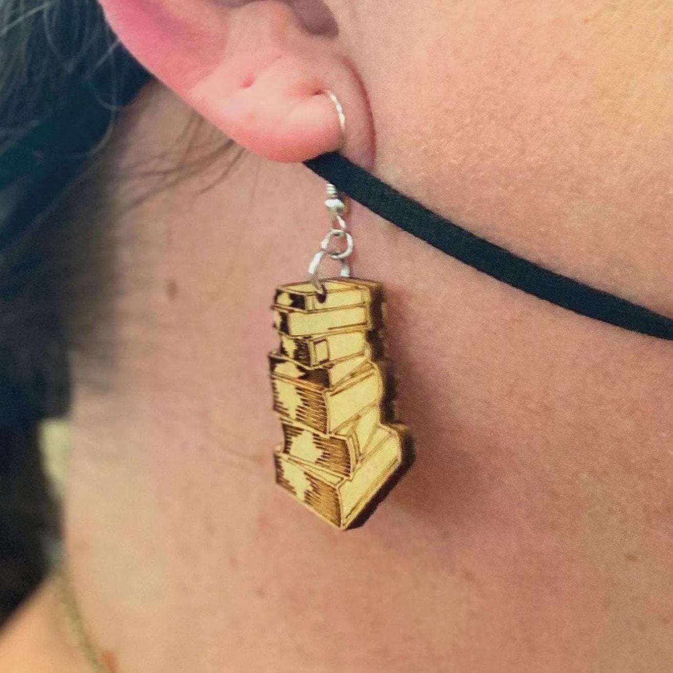 Close-up of natural wood stacked book dangle earring being worn, showing detailed engraved book design and lightweight size