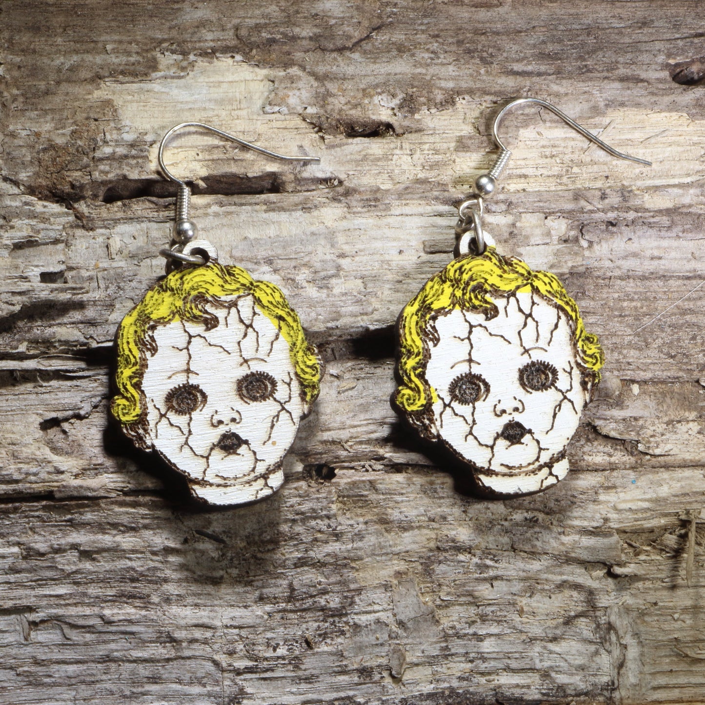Handcrafted creepy cracked doll head wooden dangle earrings featuring vintage porcelain-style doll faces with cracked details and eerie expressions. Lightweight laser-cut wooden earrings with hypoallergenic .925 sterling silver hooks, perfect for Halloween lovers, horror fans, haunted house actors, gothic fashion, creepy doll collectors, and spooky statement jewelry.