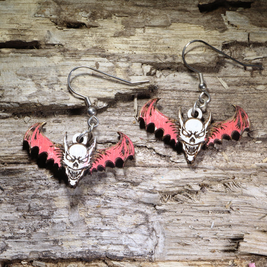 Demon skull bat wooden dangle earrings featuring a sinister horned skull with outstretched bat wings and gothic horror details. Lightweight hand-painted wooden earrings with hypoallergenic .925 sterling silver hooks, perfect for horror fans, gothic fashion, Halloween, occult-inspired style, and spooky statement jewelry.