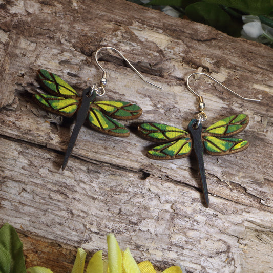 Dragonfly-shaped earrings on a wooden surface with green leaves.