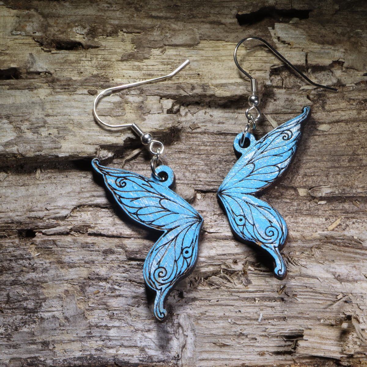 Fairy wing wooden dangle earrings featuring detailed hand-painted wings in blue with whimsical swirling accents. Lightweight fantasy earrings with hypoallergenic .925 sterling silver hooks, perfect for fairy lovers, fantasy fans, cottagecore style, renaissance festival outfits, and magical jewelry gifts.