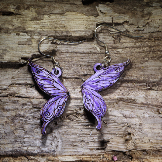 Fairy wing wooden dangle earrings featuring detailed hand-painted wings in purple with whimsical swirling accents. Lightweight fantasy earrings with hypoallergenic .925 sterling silver hooks, perfect for fairy lovers, fantasy fans, cottagecore style, renaissance festival outfits, and magical jewelry gifts.
