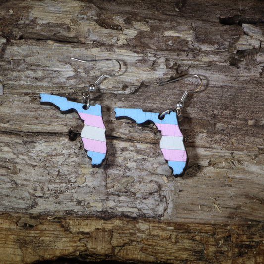 Hand-painted wooden Florida transgender pride dangle earrings featuring the Florida state silhouette with pink, blue, and white transgender pride stripes, hypoallergenic sterling silver hooks, and lightweight LGBTQ+ state pride jewelry by Cate's Concepts.