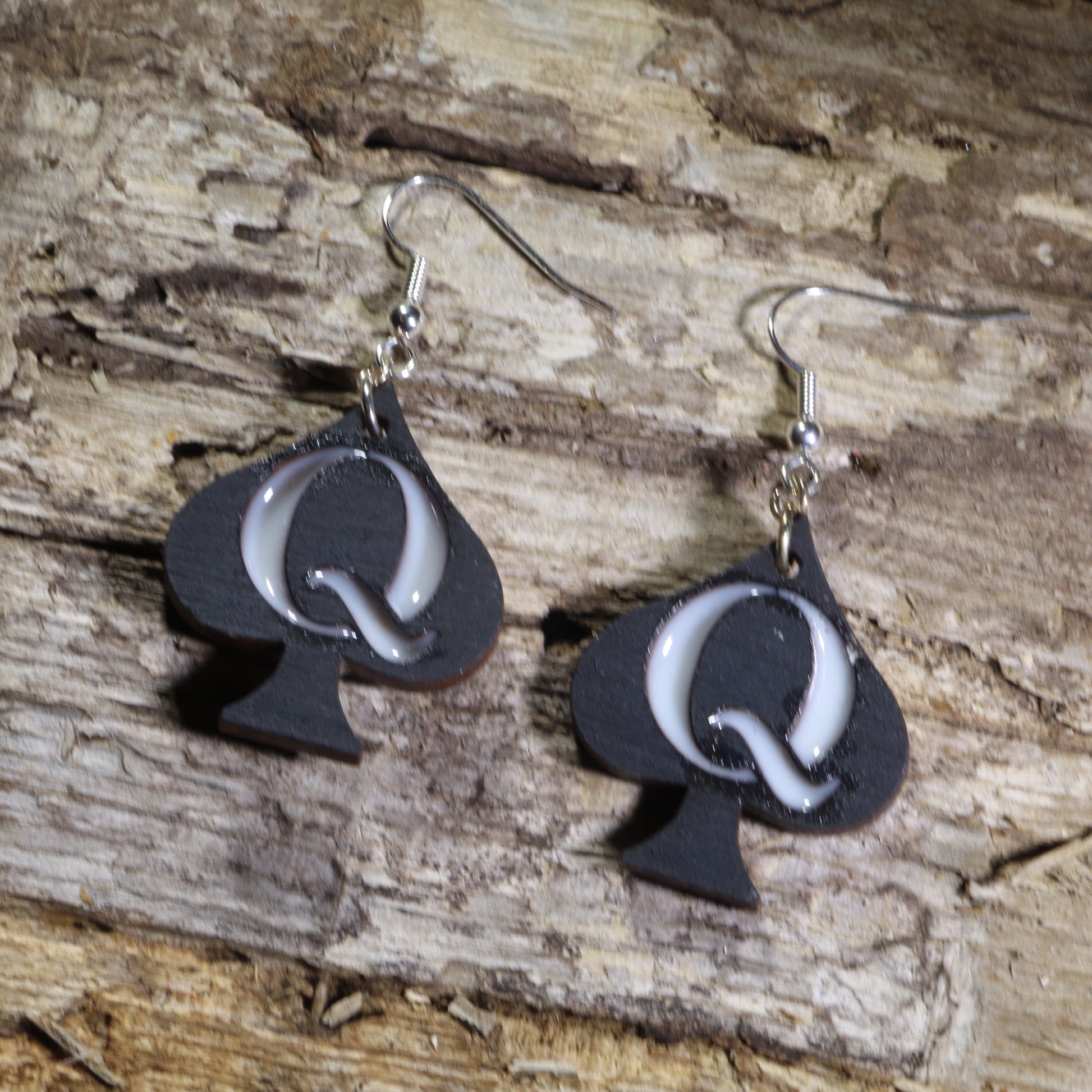 Hand-painted black wooden Queen of Spades dangle earrings featuring raised white resin "Q" lettering on hypoallergenic .925 sterling silver hooks. Lightweight card game–inspired statement jewelry for playing card enthusiasts, poker fans, and unique accessory lovers.