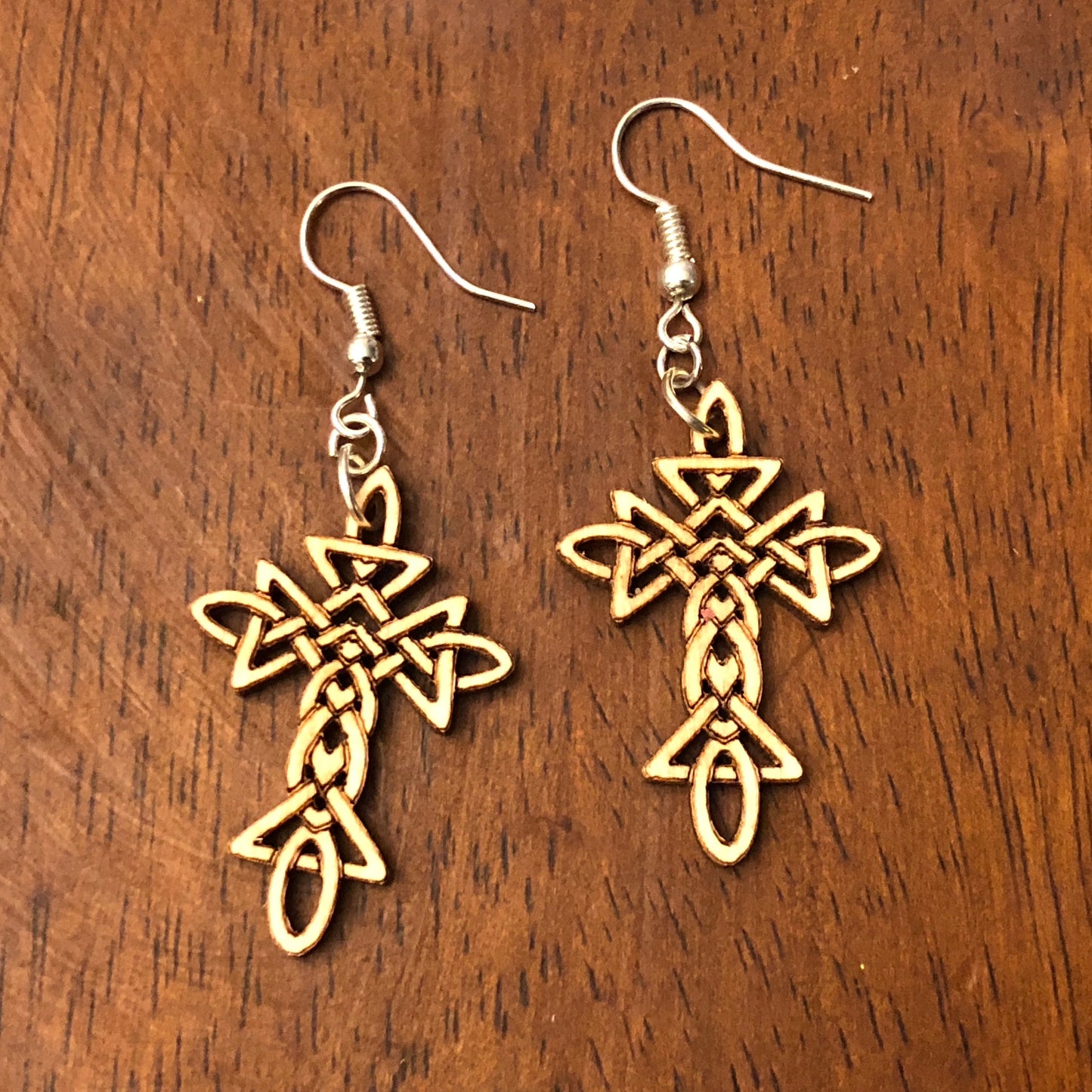 Hand-painted wooden Celtic cross dangle earrings with an intricate Celtic knot pattern on hypoallergenic .925 sterling silver hooks, displayed on a wood tabletop. Lightweight Christian faith jewelry inspired by Irish and Celtic heritage, perfect for church, Easter, everyday wear, and meaningful gifts.