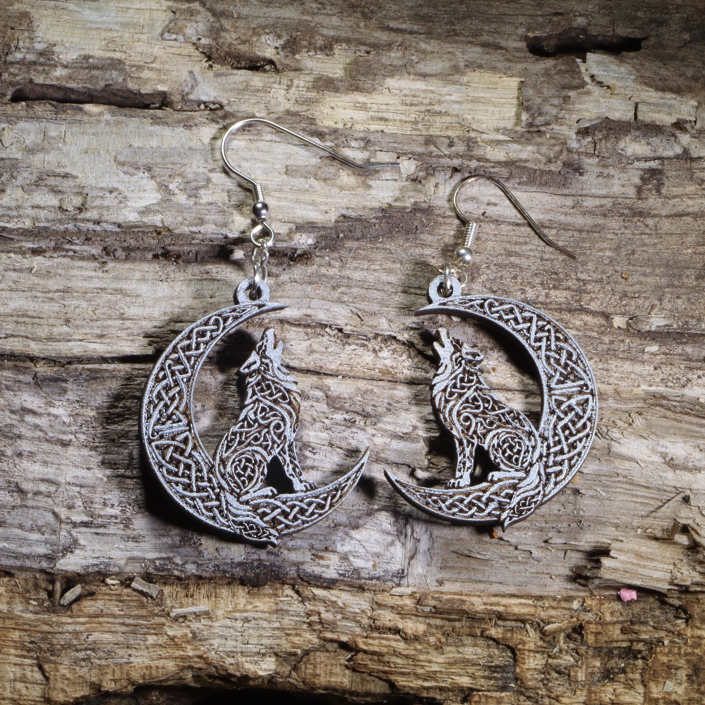 Hand-painted wooden Celtic wolf dangle earrings featuring an intricately detailed howling wolf within a Celtic knot crescent moon on hypoallergenic .925 sterling silver hooks. Lightweight Celtic jewelry for wolf lovers, pagan and Wiccan enthusiasts, nature lovers, mythology fans, and admirers of Celtic art and folklore.