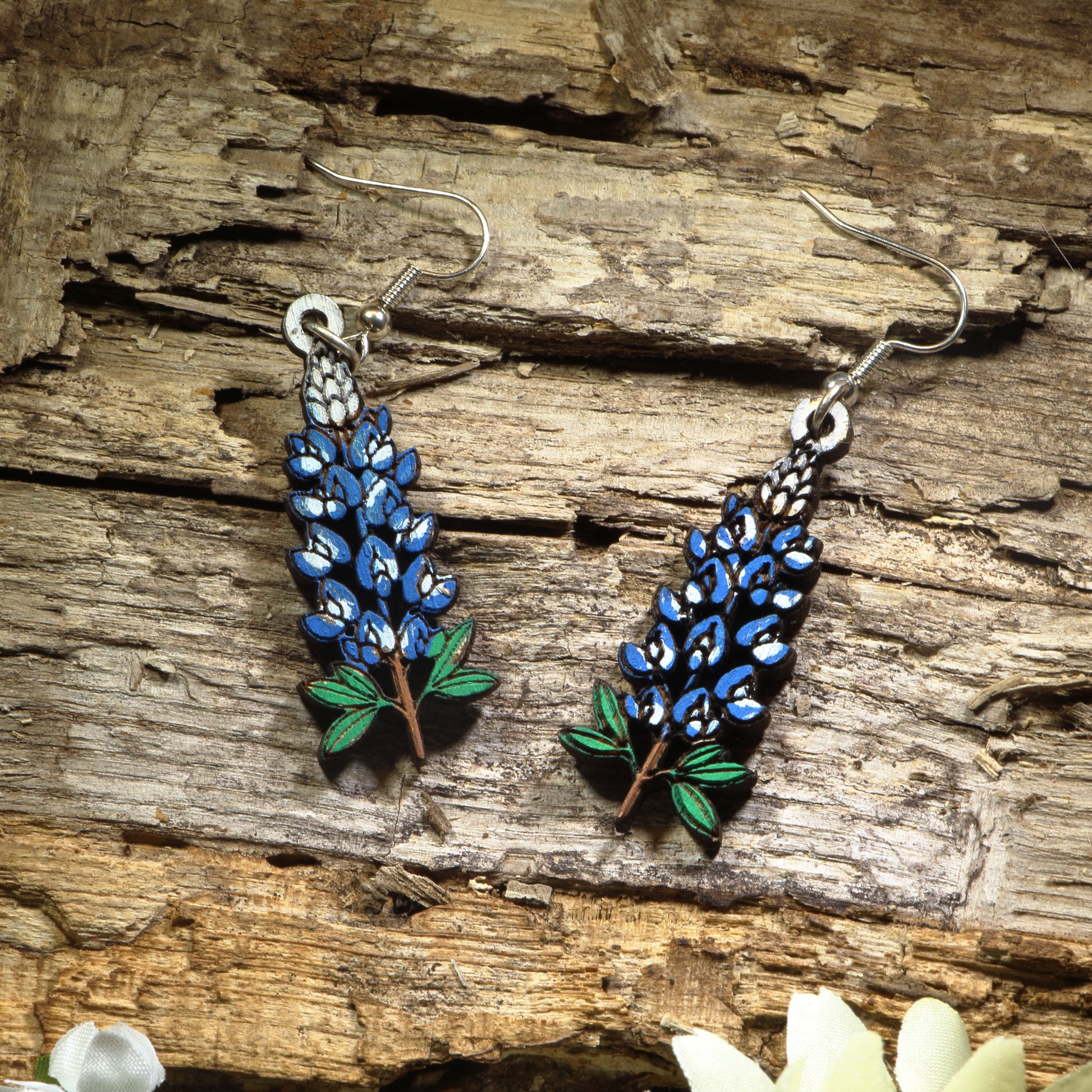 Hand-painted wooden Texas Bluebonnet dangle earrings featuring the iconic blue state flower of Texas with vibrant floral details. Crafted from lightweight wood with hypoallergenic .925 sterling silver hooks, these artisan earrings are perfect for Texas pride, wildflower lovers, spring festivals, Bluebonnet season, nature enthusiasts, travel souvenirs, and anyone who loves colorful botanical jewelry inspired by the Lone Star State.