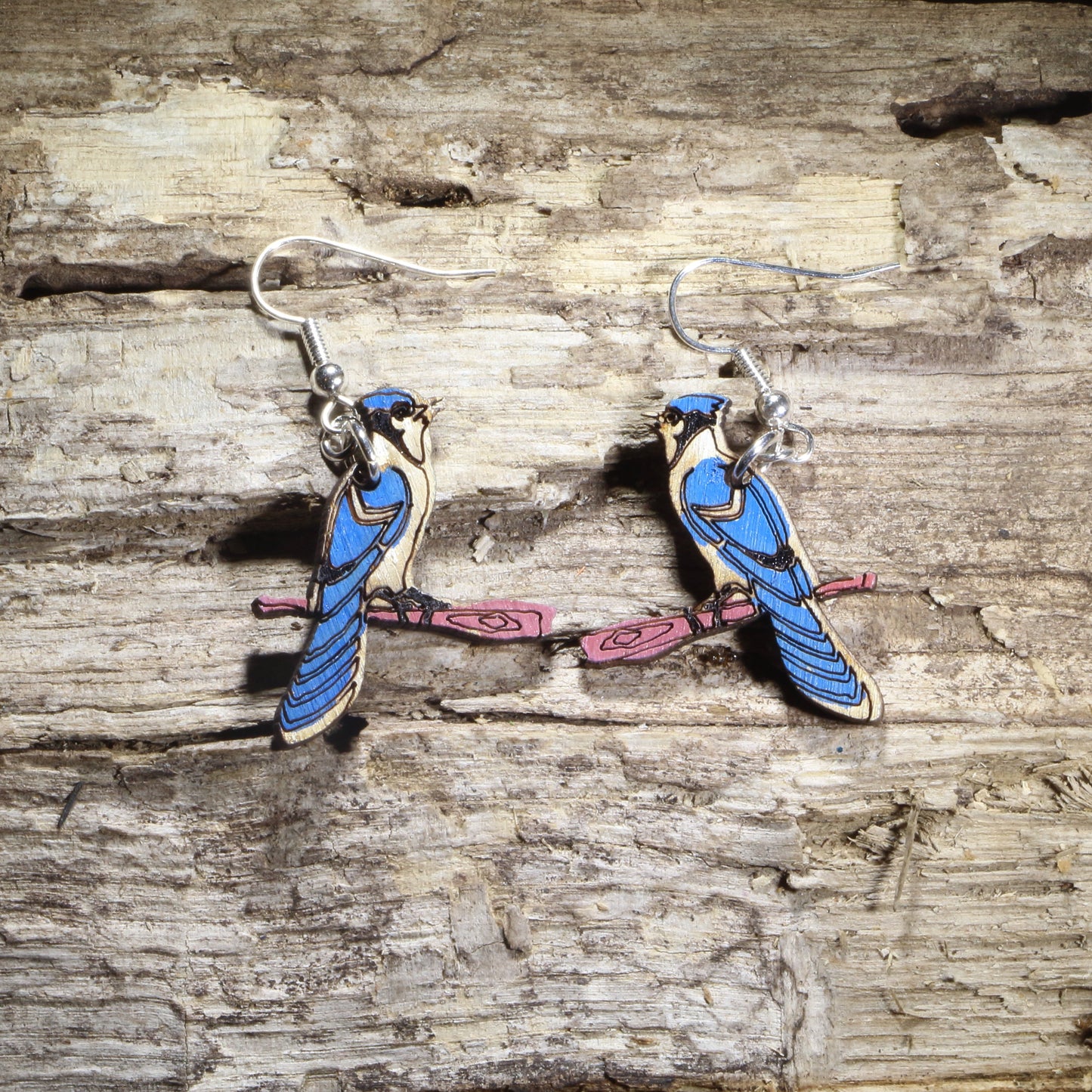 Hand-painted wooden blue jay dangle earrings featuring two blue jays perched on pink tree branches with hypoallergenic .925 sterling silver hooks. Lightweight bird lover jewelry inspired by backyard songbirds, perfect for nature enthusiasts, birdwatchers, and wildlife gifts.