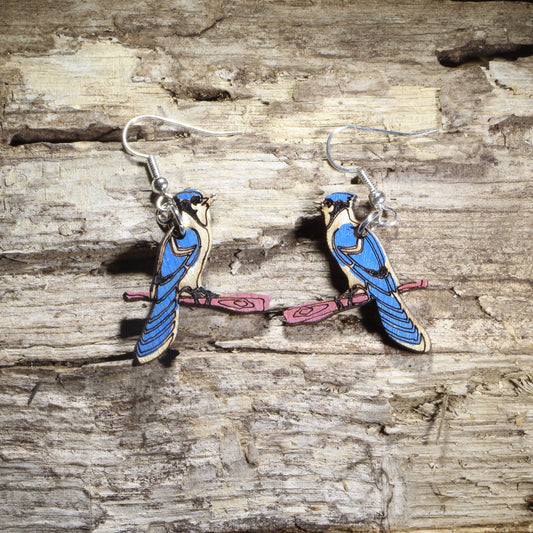 Hand-painted wooden blue jay dangle earrings featuring two blue jays perched on pink tree branches with hypoallergenic .925 sterling silver hooks. Lightweight bird lover jewelry inspired by backyard songbirds, perfect for nature enthusiasts, birdwatchers, and wildlife gifts.