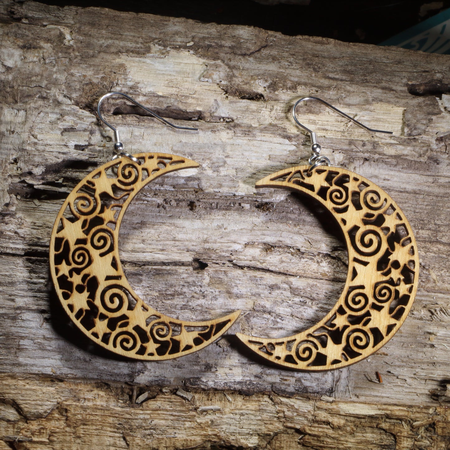 Hand-painted wooden cutout crescent moon dangle earrings featuring an intricate celestial cutout design with stars and swirling patterns on hypoallergenic .925 sterling silver hooks. Lightweight moon jewelry for astronomy lovers, astrology enthusiasts, witches, pagans, celestial decor fans, and lovers of mystical accessories.