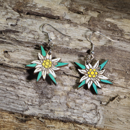 Hand-painted wooden edelweiss flower dangle earrings featuring white alpine blossoms with yellow centers and teal accents on hypoallergenic .925 sterling silver hooks. Lightweight floral jewelry perfect for nature lovers, hikers, alpine flower enthusiasts, Swiss and Austrian heritage, and botanical-inspired accessories.