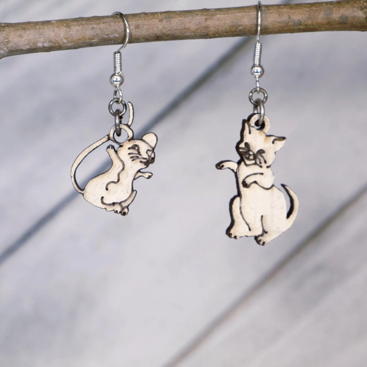 Hand-painted wooden mismatched cat and mouse dangle earrings featuring a playful white cat reaching toward a smiling mouse on hypoallergenic .925 sterling silver hooks. Lightweight animal jewelry displayed hanging from a branch for cat lovers, mouse enthusiasts, pet owners, and fans of whimsical accessories.