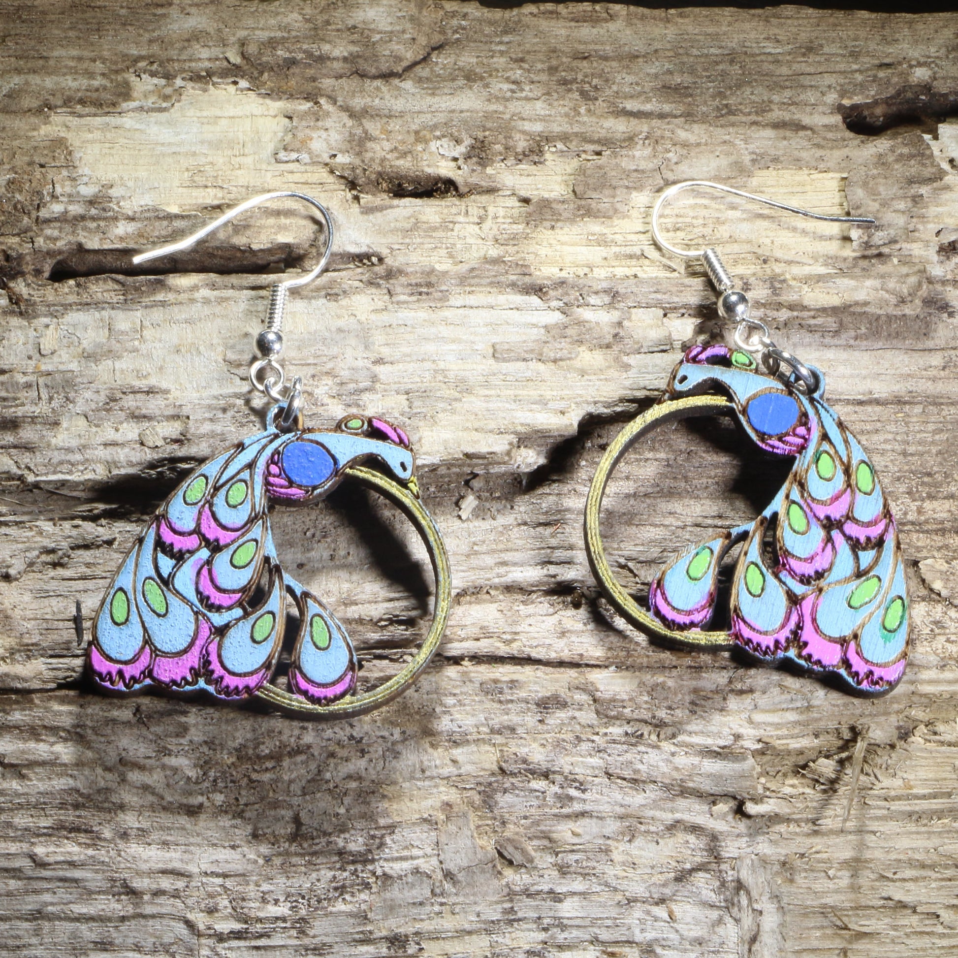 Hand-painted wooden peacock dangle earrings featuring a colorful stylized peacock with vibrant blue, purple, and green feathers and an open circular tail design on hypoallergenic .925 sterling silver hooks. Lightweight bird jewelry for peacock lovers, birdwatchers, nature enthusiasts, and fans of colorful statement accessories.