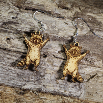 Hand-painted wooden raccoon dangle earrings featuring an adorable raccoon with raised paws and engraved fur details on hypoallergenic .925 sterling silver hooks. Lightweight woodland animal jewelry perfect for raccoon lovers, wildlife enthusiasts, and nature-inspired accessories