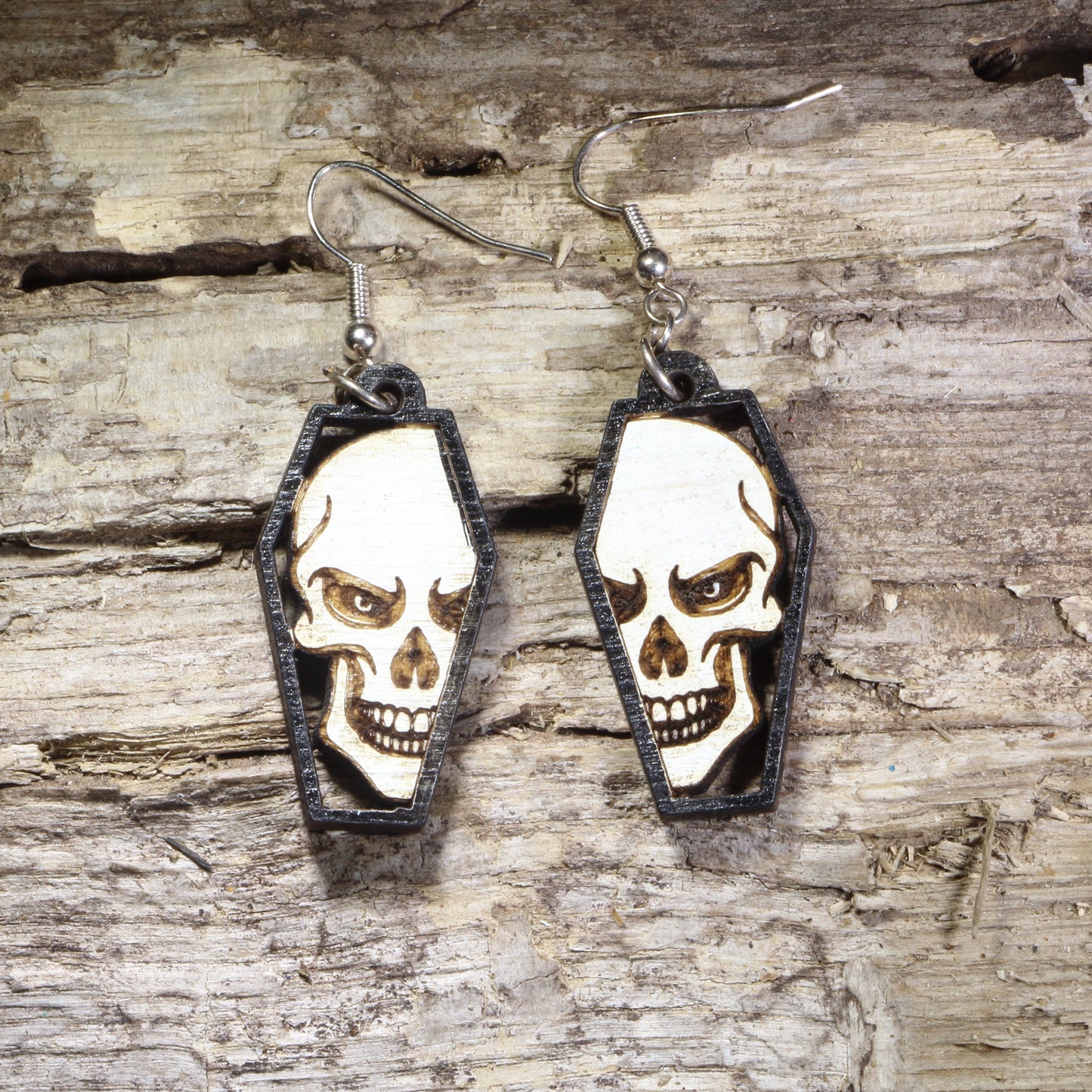Hand-painted wooden skull in coffin dangle earrings featuring a detailed gothic skull framed inside a black coffin on hypoallergenic .925 sterling silver hooks. Lightweight gothic jewelry for Halloween, spooky style, horror fans, alternative fashion, and skull lovers.