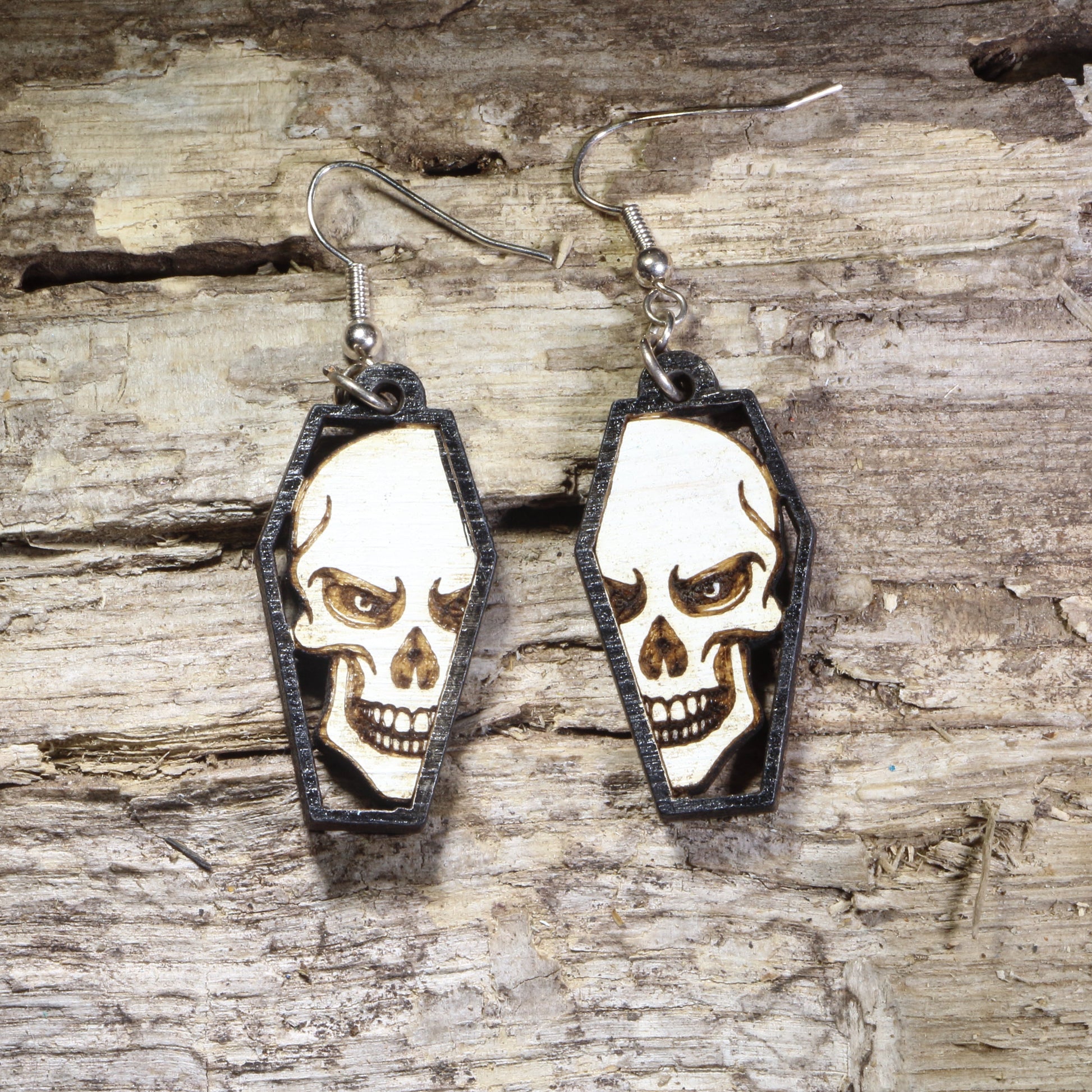 Hand-painted wooden skull in coffin dangle earrings featuring a detailed gothic skull framed inside a black coffin on hypoallergenic .925 sterling silver hooks. Lightweight gothic jewelry for Halloween, spooky style, horror fans, alternative fashion, and skull lovers.