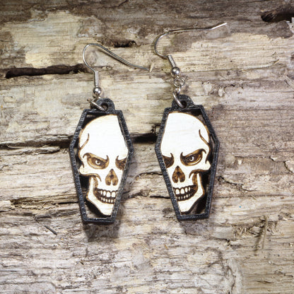 Hand-painted wooden skull in coffin dangle earrings featuring a detailed gothic skull framed inside a black coffin on hypoallergenic .925 sterling silver hooks. Lightweight gothic jewelry for Halloween, spooky style, horror fans, alternative fashion, and skull lovers.