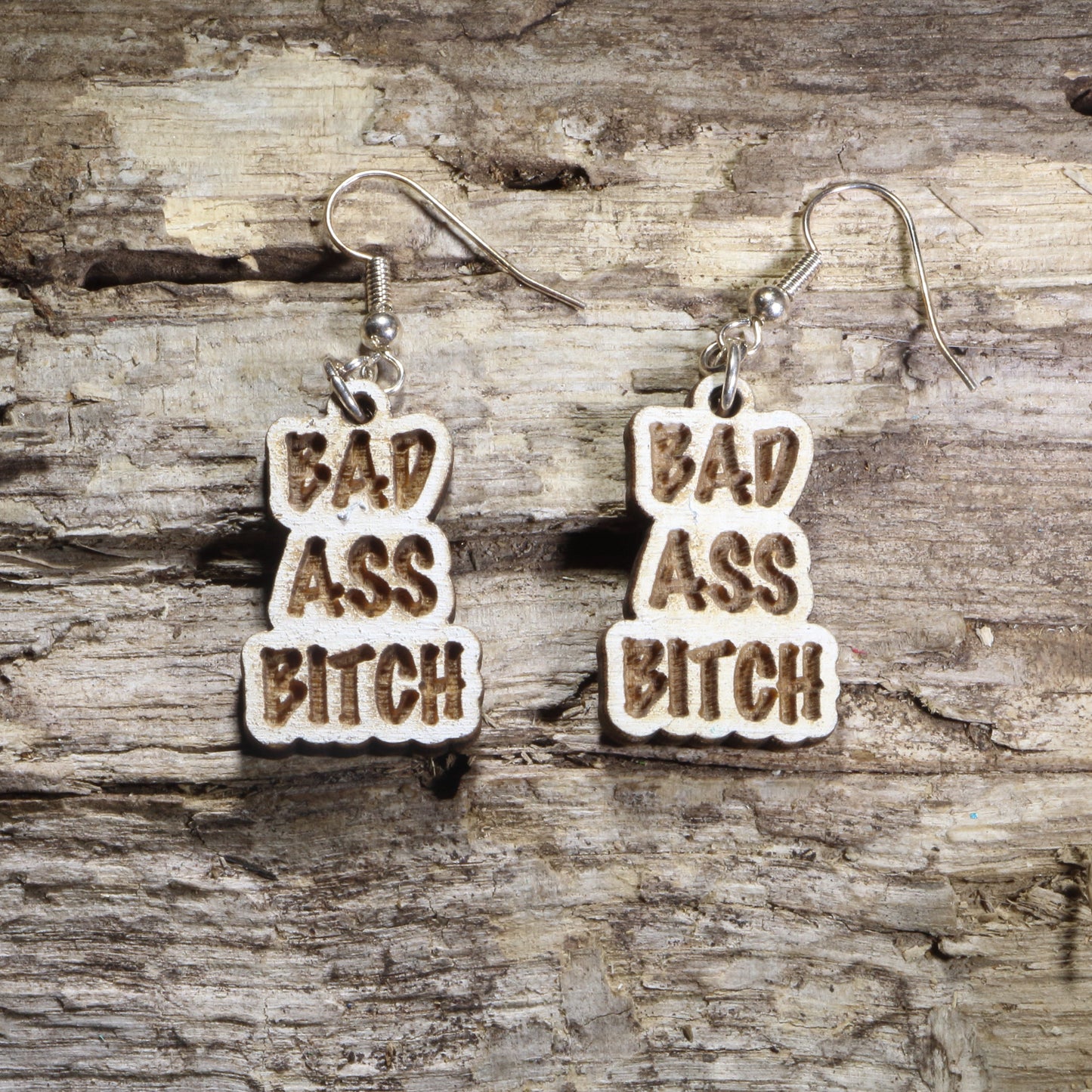 Handcrafted "Bad Ass Bitch" wooden dangle earrings featuring bold engraved lettering in a statement design. Lightweight laser-cut wooden earrings with hypoallergenic .925 sterling silver hooks, perfect for confident women, funny adult humor, bachelorette parties, girls' nights, and bold statement fashion.