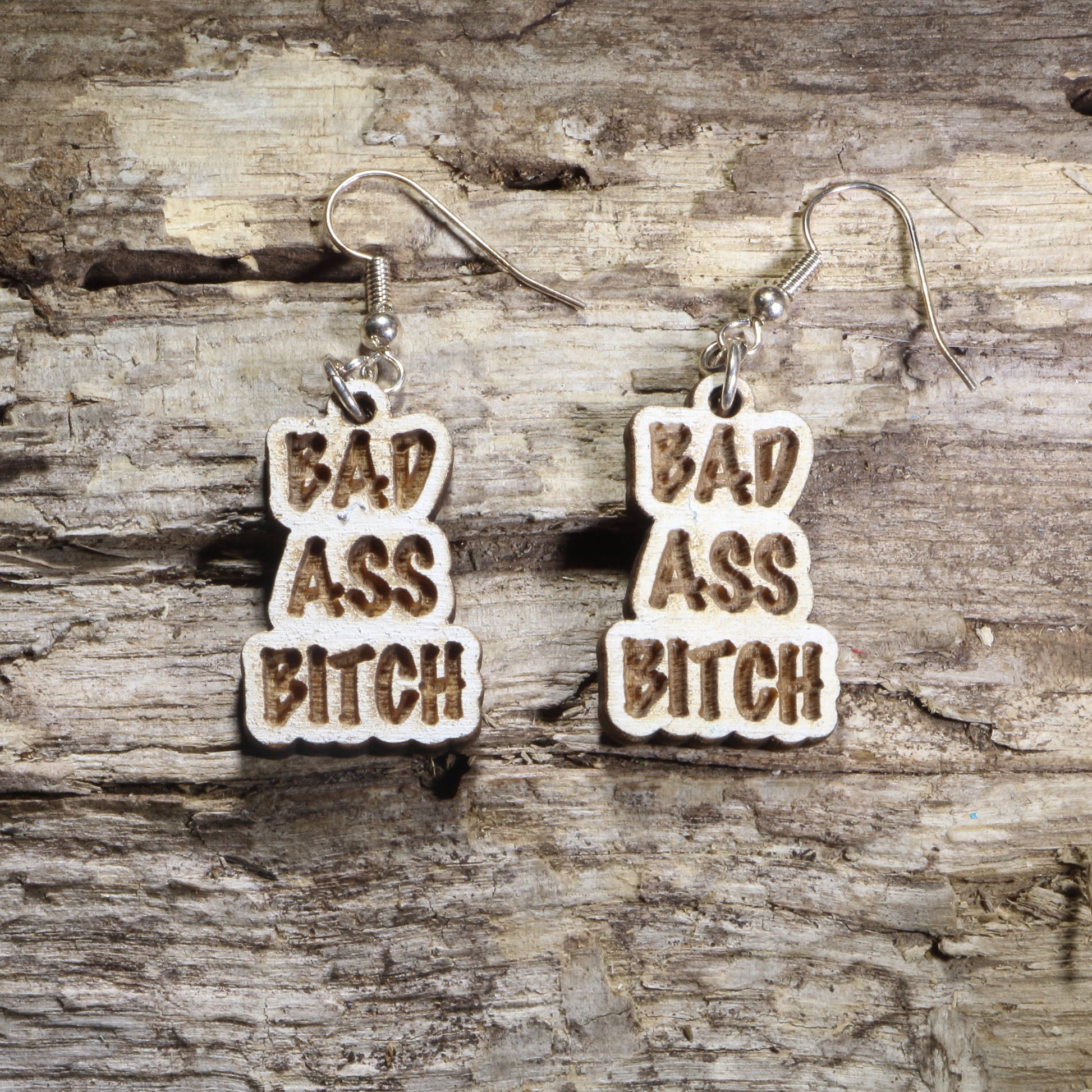Handcrafted "Bad Ass Bitch" wooden dangle earrings featuring bold engraved lettering in a statement design. Lightweight laser-cut wooden earrings with hypoallergenic .925 sterling silver hooks, perfect for confident women, funny adult humor, bachelorette parties, girls' nights, and bold statement fashion.