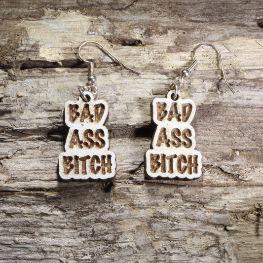 Handcrafted "Bad Ass Bitch" wooden dangle earrings featuring bold engraved lettering in a statement design. Lightweight laser-cut wooden earrings with hypoallergenic .925 sterling silver hooks, perfect for confident women, funny adult humor, bachelorette parties, girls' nights, and bold statement fashion.
