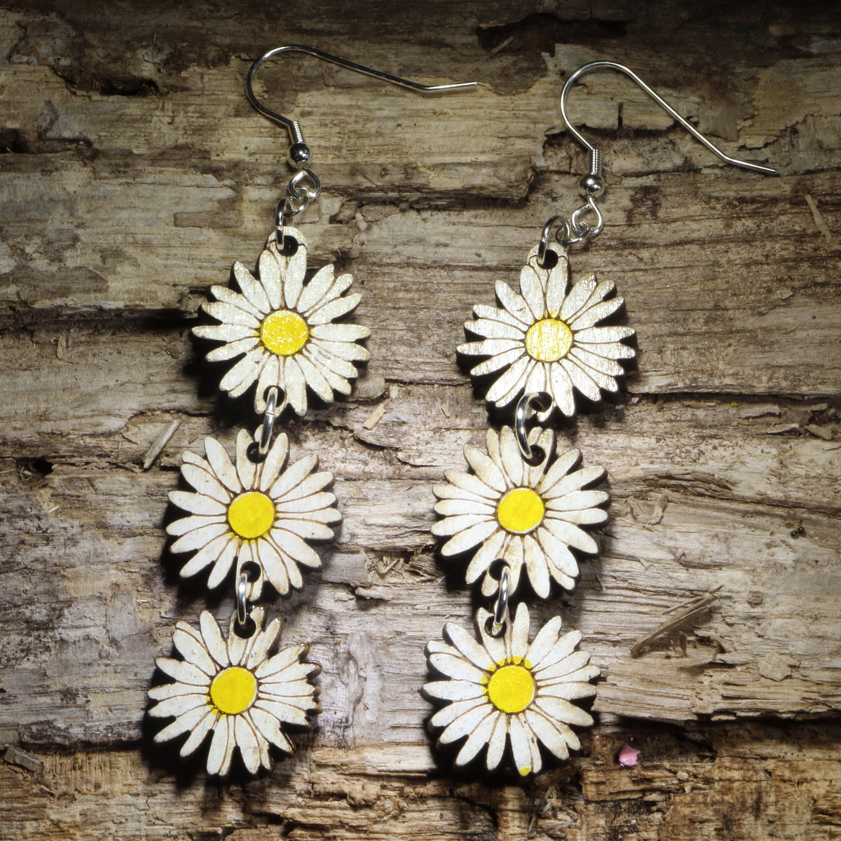 Handcrafted daisy chain wooden dangle earrings featuring three hand-painted white daisies with bright yellow centers linked together for graceful movement. Lightweight laser-cut floral earrings with hypoallergenic .925 sterling silver hooks, perfect for cottagecore fashion, wildflower lovers, spring and summer outfits, botanical jewelry, garden enthusiasts, and nature-inspired accessories
