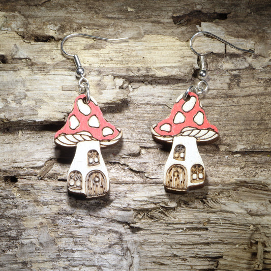 Handcrafted fairy mushroom house wooden dangle earrings featuring whimsical red spotted mushroom cottages with tiny windows and doors. Lightweight hand-painted wooden earrings with hypoallergenic .925 sterling silver hooks, perfect for cottagecore fashion, fairy garden lovers, fantasy enthusiasts, woodland décor fans, whimsical gifts, and enchanted forest accessories.