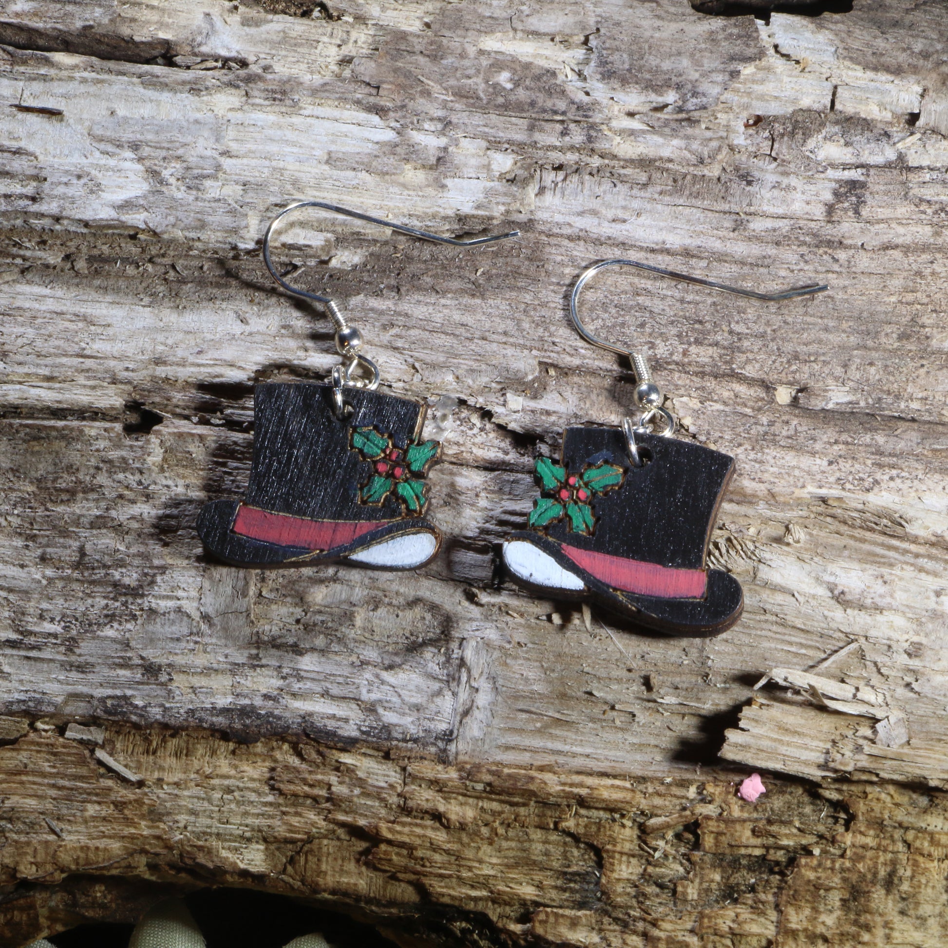 Handcrafted wooden snowman hat dangle earrings featuring classic black top hats decorated with festive holly leaves and red hatbands. These lightweight Christmas earrings are finished with hypoallergenic .925 sterling silver hooks, making them a fun holiday accessory for Christmas parties, winter celebrations, festive outfits, and seasonal gift giving.