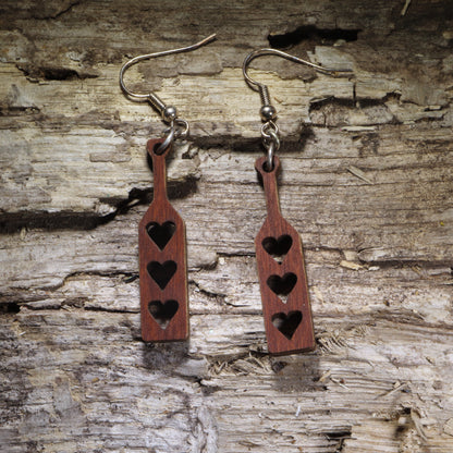 Handcrafted wooden spanking paddle dangle earrings featuring three heart-shaped cutouts in a classic adult paddle design. Lightweight laser-cut wooden earrings with hypoallergenic .925 sterling silver hooks, perfect for BDSM enthusiasts, kink fashion, fetish events, adult humor, playful gifts, and handmade novelty jewelry.