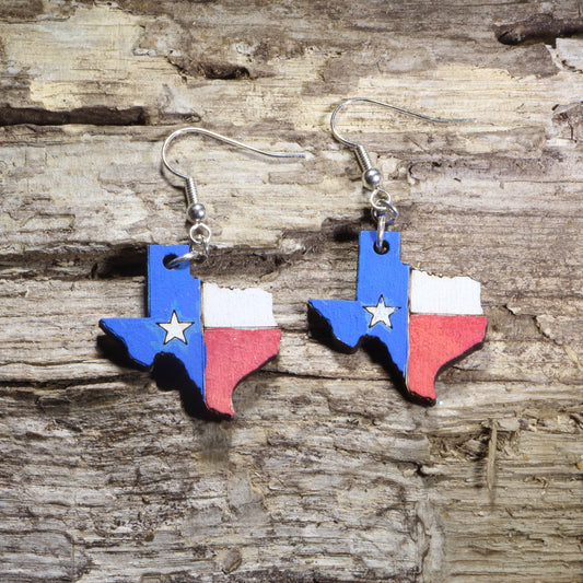 Handmade Texas flag wooden dangle earrings featuring the outline of the state of Texas painted with the iconic Texas flag and Lone Star. Lightweight Texas earrings crafted from wood with hypoallergenic .925 sterling silver hooks, perfect for Texas pride, Texans, western fashion, state souvenirs, patriotic celebrations, and unique handmade jewelry.