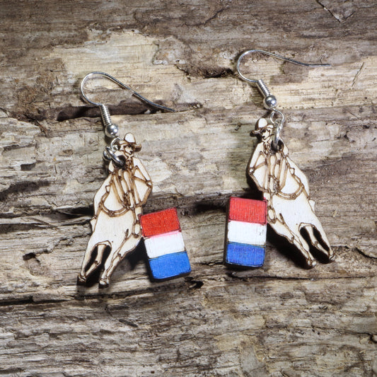 Handmade barrel racing wooden dangle earrings featuring a laser-cut western saddle with a red, white, and blue racing barrel charm. Lightweight patriotic rodeo earrings crafted from wood with hypoallergenic .925 sterling silver hooks, perfect for barrel racers, horse lovers, equestrians, western fashion, and country lifestyle enthusiasts.