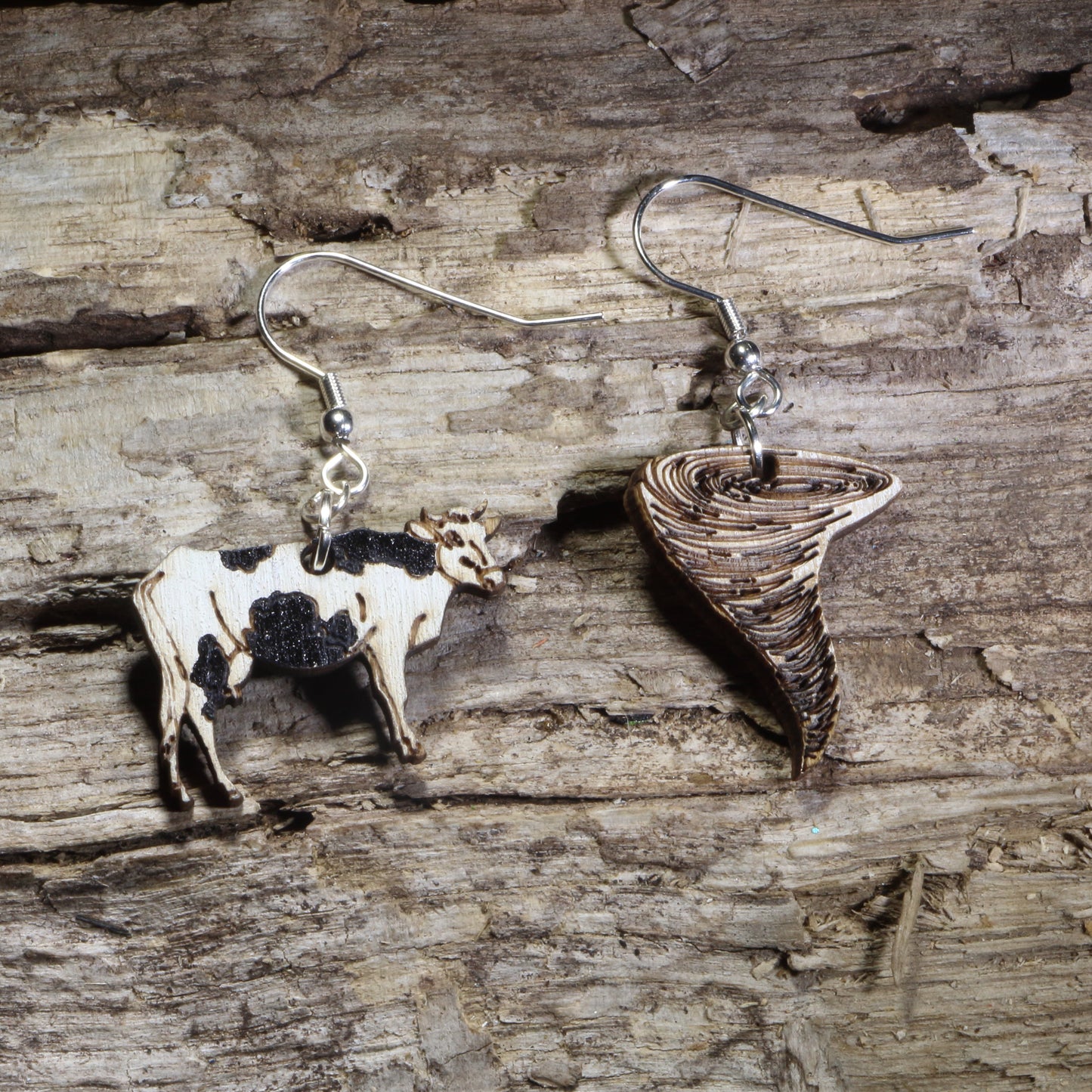 Handmade mismatched wooden dangle earrings featuring a black and white cow and a tornado crafted from lightweight laser-cut wood with hypoallergenic .925 sterling silver hooks. Funny farm jewelry inspired by rural life, storm chasing, Oklahoma humor, country living, and unique novelty gifts.