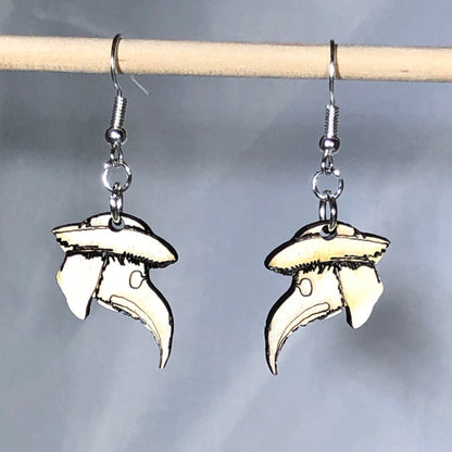 Handmade wooden plague doctor mask dangle earrings with engraved details and a classic beaked mask design on hypoallergenic .925 sterling silver hooks, displayed hanging against a soft blue background. Lightweight gothic jewelry for Halloween lovers, dark academia enthusiasts, horror fans, and historical costume collectors.
