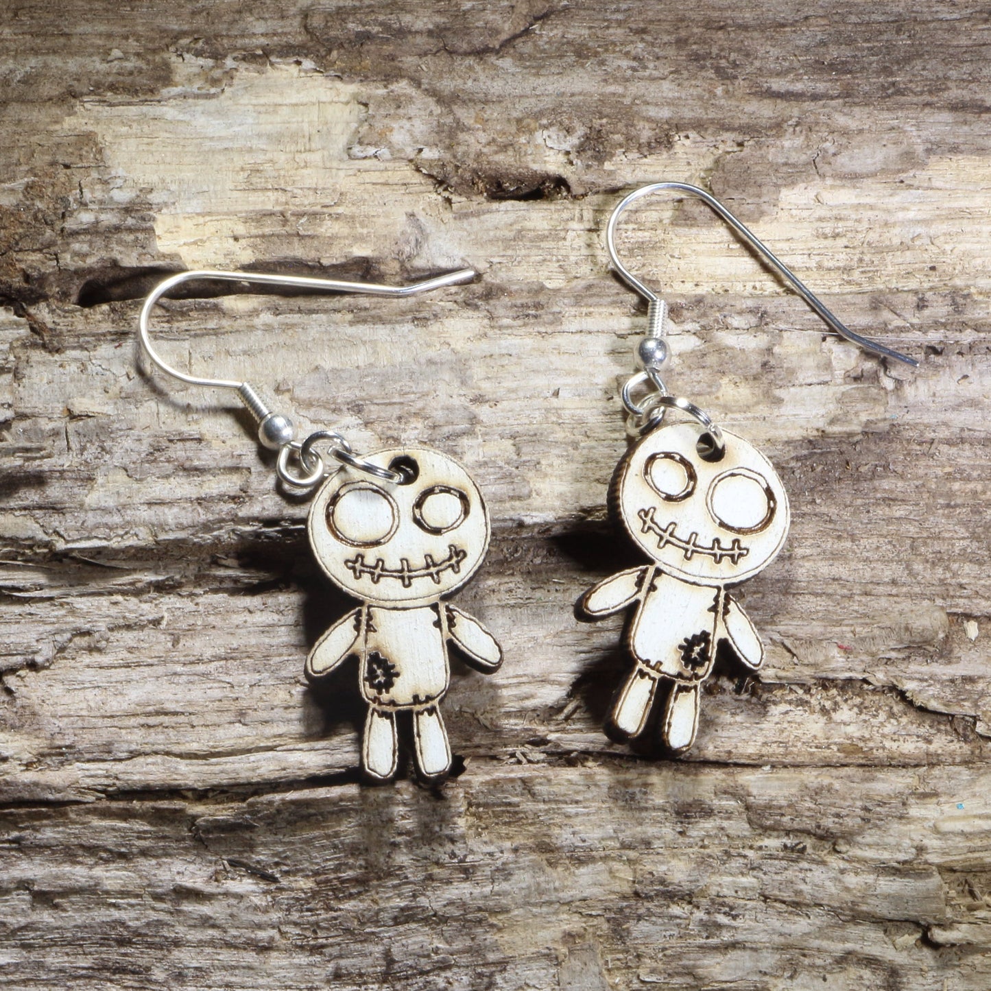 Handmade wooden voodoo doll dangle earrings featuring a stitched rag doll design with oversized eyes and patch details. Lightweight gothic-inspired earrings crafted from wood with hypoallergenic .925 sterling silver hooks, perfect for Halloween, spooky style, horror fans, gothic fashion, and lovers of creepy cute jewelry.