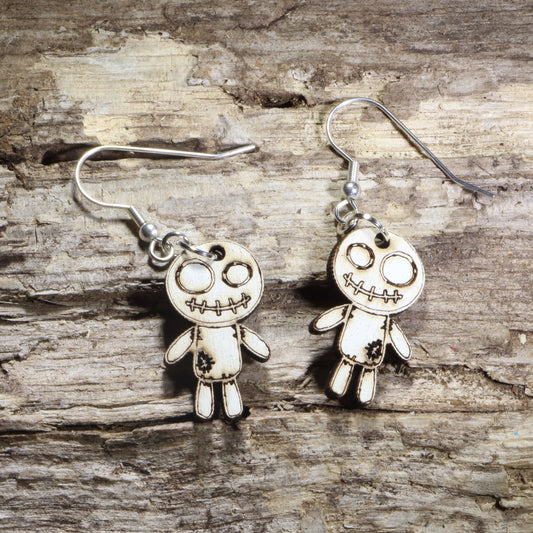 Handmade wooden voodoo doll dangle earrings featuring a stitched rag doll design with oversized eyes and patch details. Lightweight gothic-inspired earrings crafted from wood with hypoallergenic .925 sterling silver hooks, perfect for Halloween, spooky style, horror fans, gothic fashion, and lovers of creepy cute jewelry.