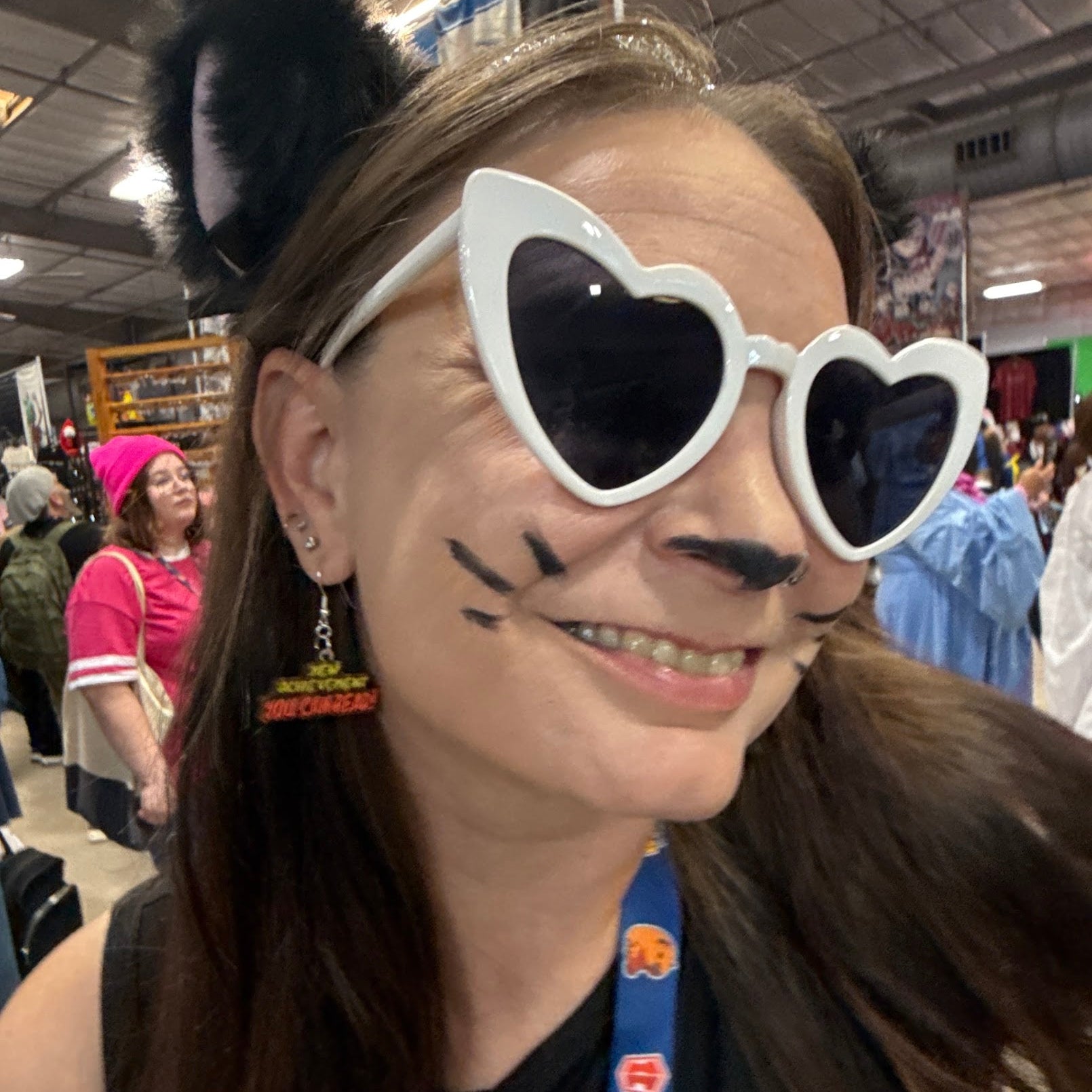 Woman wearing handcrafted "New Achievement You Can Read" wooden dangle earrings at a comic convention, featuring a layered green and orange marquee-style design. Lifestyle photo showcasing lightweight statement earrings with hypoallergenic .925 sterling silver hooks, perfect for Halloween fans, spooky fashion lovers, cosplay, and horror movie enthusiasts.
