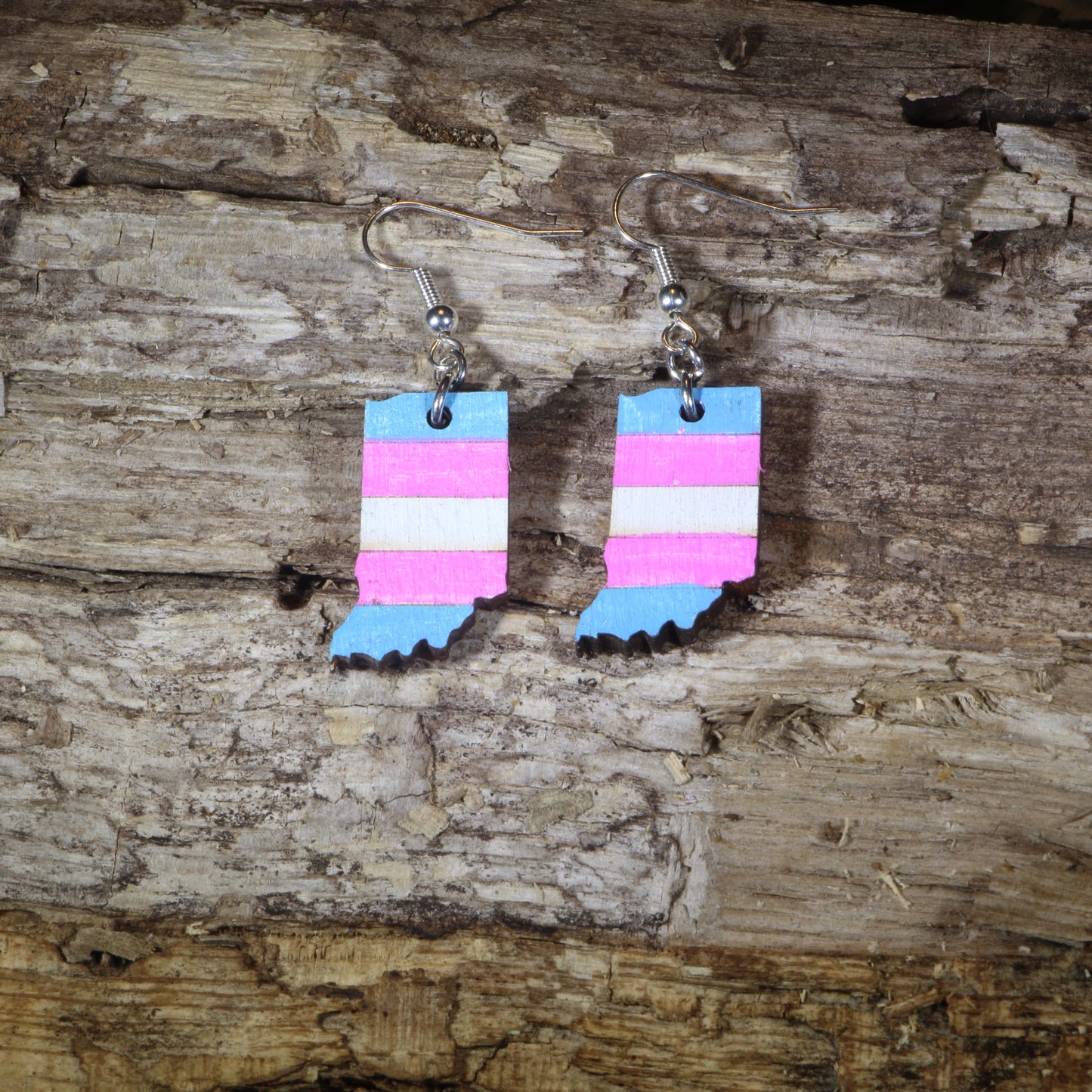 Hand-painted wooden Indiana transgender pride dangle earrings featuring the Indiana state silhouette with pink, blue, and white transgender pride stripes, hypoallergenic sterling silver hooks, and lightweight LGBTQ+ state pride jewelry by Cate's Concepts.
