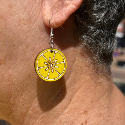 Close-up of hand-painted wooden lemon slice dangle earrings with hypoallergenic silver hooks, citrus fruit summer jewelry by Cate’s Concepts